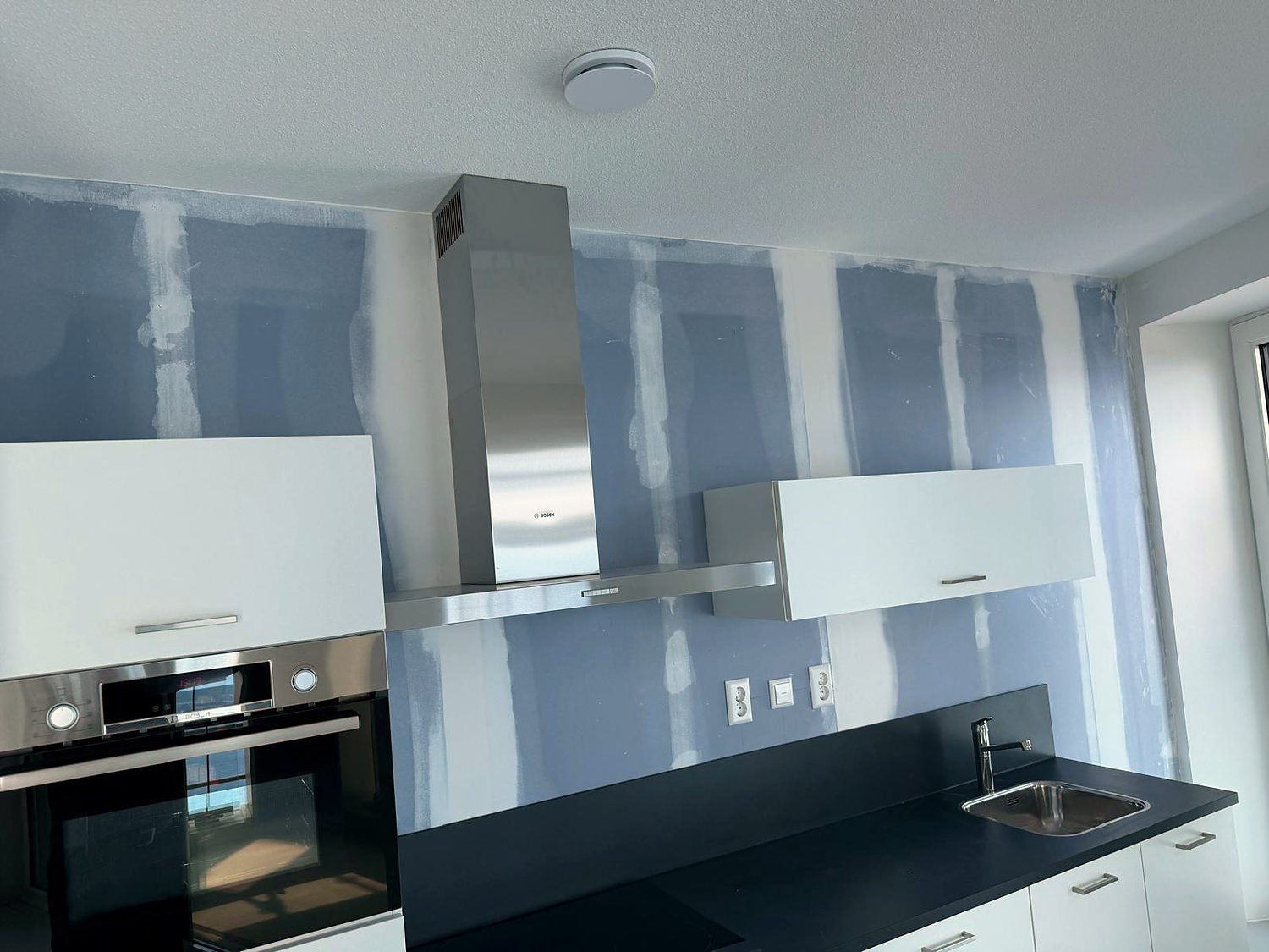 Keuken in een appartement tijdens de afbouw: de afzuigkap en de bovenkasten hangen, de wanden zijn geplaat en de naden zijn gevlakt