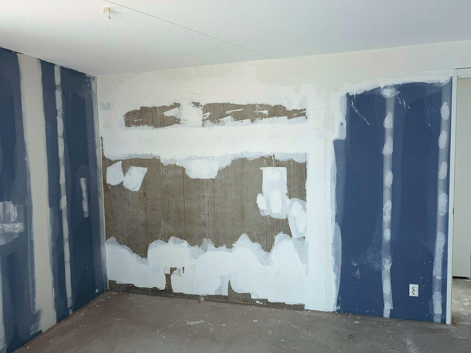 Kamer in ruwbouwfase met gipswanden waarvan de naden zijn afgeplakt en gevlakt, naast een deels afgehakte betonwand