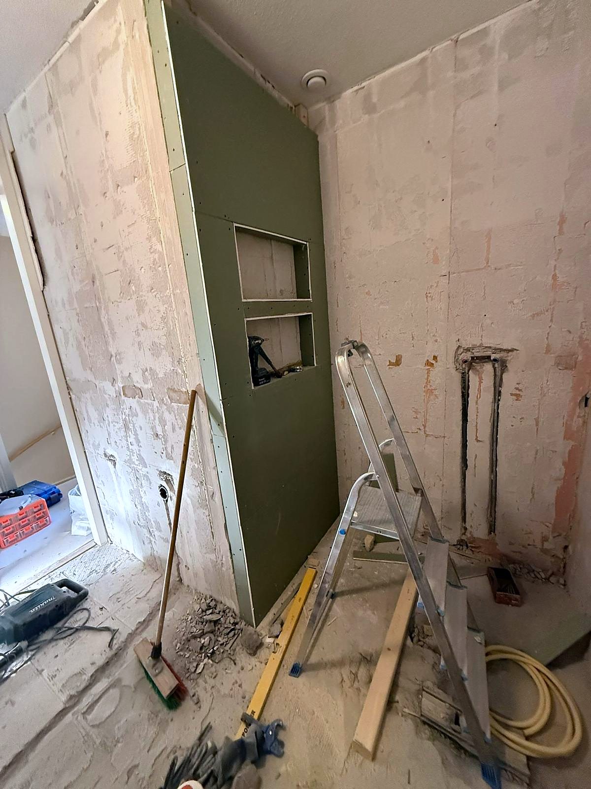 Dezelfde badkamer in de ruwbouwfase, met een nieuwe voorzetwand van vochtwerende plaat, een ingebouwde nis en verse leidingsleuven in de muur