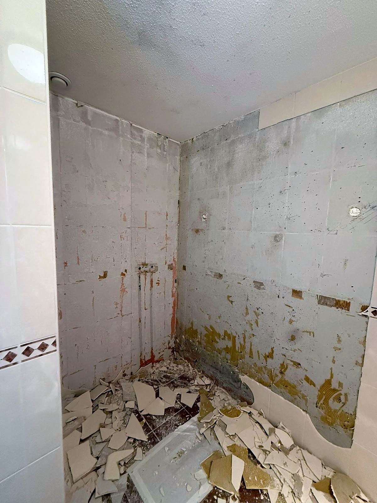 Badkamer tijdens de sloop: het oude wandtegelwerk is eraf gehakt tot op de ondergrond en de scherven liggen op de vloer