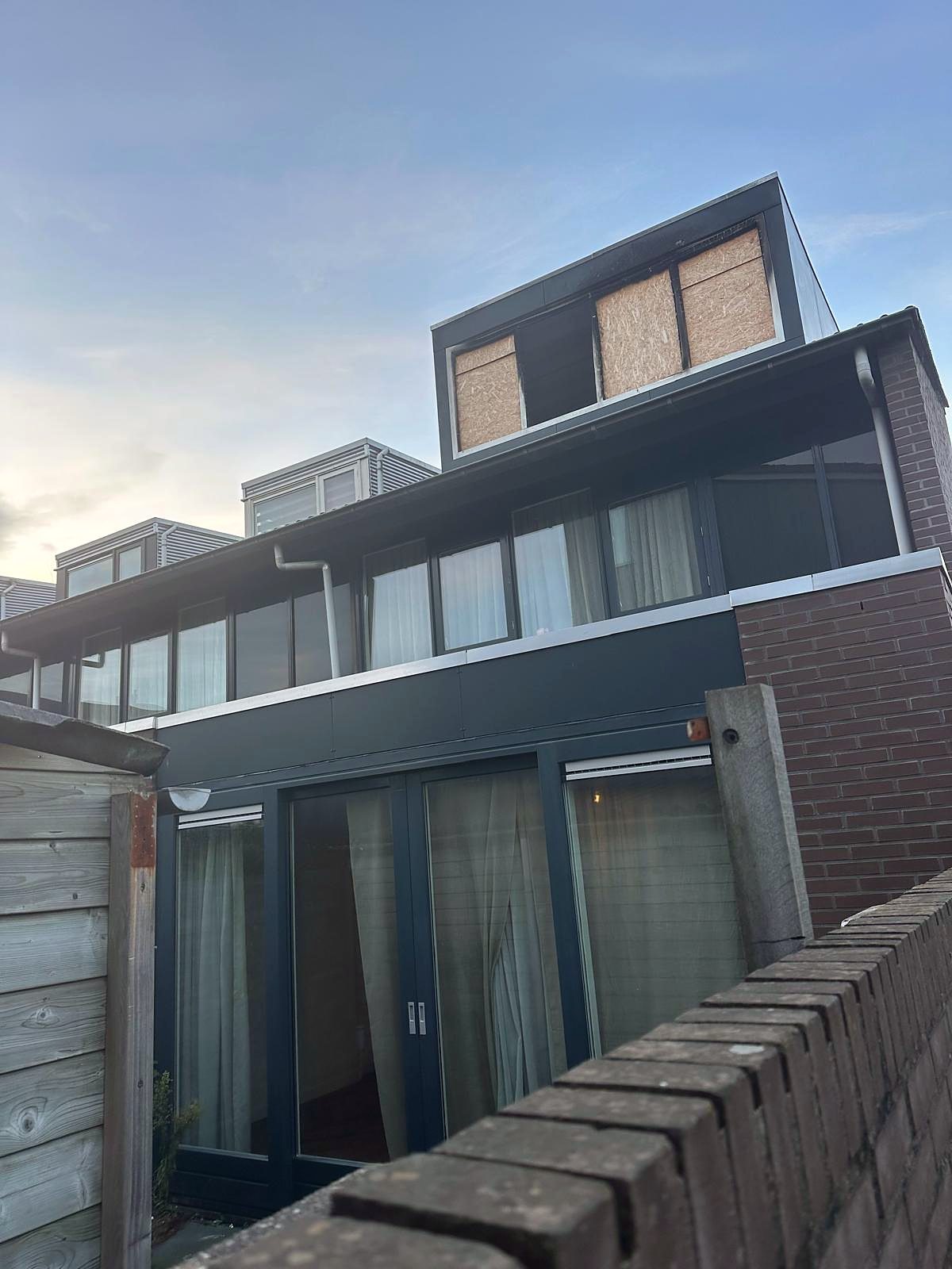 Achtergevel van een woning met een nieuwe dakopbouw in antracietgrijze beplating, waarvan de kozijnen nog dichtgezet zijn met plaatmateriaal