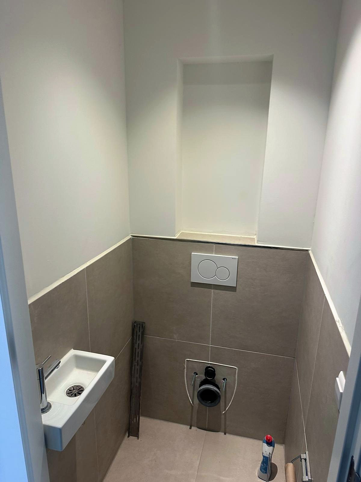 Toilet met halfhoog tegelwerk in betonlook, een inbouwreservoir met bedieningsplaat, een fonteintje en een nis in de wand